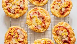 Mini pizze z serka wiejskiego, z kukurydzą i kawałkami mięsa, ułożone na metalowej kratce.