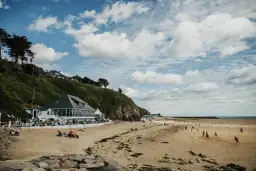 Plage normande avec restaurant en bord de mer, gens sur le sable et terrain de volley.