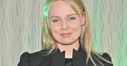 Patrycja Redo, z niebieskimi oczami i blond włosami, uśmiecha się. W tle falista zasłona.