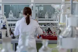 Naukowczyni w białym fartuchu pracuje w laboratorium, otoczona szkłem laboratoryjnym. Analizuje próbki, być może badając rdw-cv.