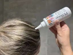 Aplikacja peelingu do skóry głowy z kwasami AHA na wilgotne włosy. Produkt w białej tubce z kolorowymi owocami.
