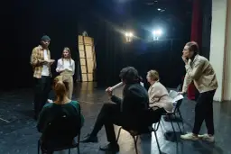 Grupa ludzi na scenie, dyskutująca o sztuce. Zastanawiają się, ile zarabia reżyser w Polsce, analizując scenariusz.