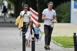 Anna Mucha z dziećmi spaceruje po chodniku. Dziewczynka w różowej sukience i chłopiec w niebieskiej koszuli idą obok.