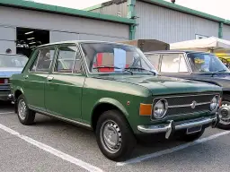Zielony fiat 128, klasyk z lat 70., zaparkowany przed budynkiem.