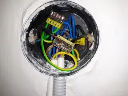 W puszce elektrycznej widać przewody: fazowy (czarny), neutralny (niebieski) i ochronny (zielono-żółty). Pytanie, czy uziemienie można podłączyć do zera, jest kluczowe dla bezpieczeństwa.