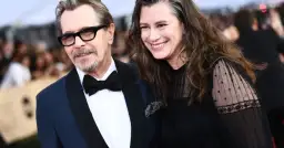 Gary Oldman z żoną, oboje uśmiechnięci, on w garniturze i okularach, ona w czarnej sukience.
