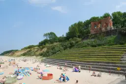 Plaża w Rewalu z ruinami na klifie. Ludzie odpoczywają na piasku, ciesząc się słońcem i widokiem. To popularne rewal atrakcje.