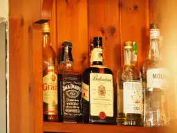 Butelki whisky na drewnianej półce. Zwróć uwagę na zmętnienie i osad w starych butelkach, by rozpoznać objawy zepsutej whisky.