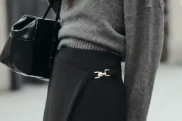 Chaqueta gris y bolso negro sobre falda negra larga con detalle dorado. Un look elegante para saber como combinar una falda negra larga.
