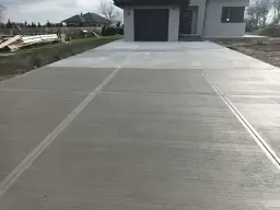 Nowy podjazd z beton stemplowany, z wyraźnymi fugami, prowadzi do nowoczesnego domu z szarą bramą garażową.