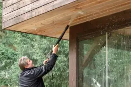 Mężczyzna myje drewnianą podbitkę myjką ciśnieniową. Woda rozpryskuje się, pokazując, czy biała podbitka się brudzi.