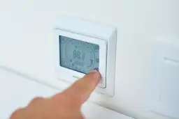 Palec naciska przycisk termostatu, ustawiając idealną temperaturę pieca gazowego.
