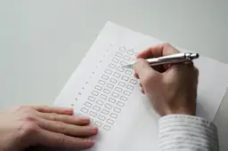 Dłoń z długopisem wypełnia ankietę z polami wyboru.
