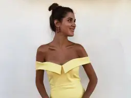 Mujer con moño alto y pendientes rojos, luciendo un vestido amarillo de hombros caídos. Ideas para combinar zapatos para vestido amarillo.