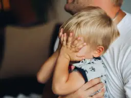 20 miesięczne dziecko budzi się w nocy, ukrywając twarz w dłoniach. Tata tuli go, próbując uspokoić.