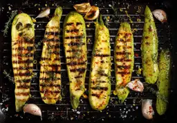 Pyszna cukinia z grilla, doprawiona czosnkiem, tymiankiem i płatkami chili, leży na ruszcie.