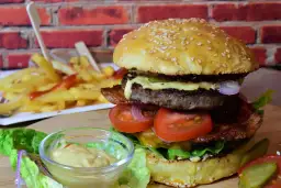 Soczysty burger z kotletem wołowym, warzywami i frytkami w tle.