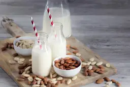 Mleko migdałowe w butelkach z czerwono-białymi słomkami, miseczki z migdałami. Idealne na dieta bez nabiału.