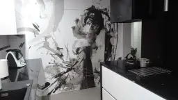 Nowoczesna kuchnia z czarnym blatem i białymi szafkami. Na ścianie artystyczny mural, który świetnie maskuje drzwi.