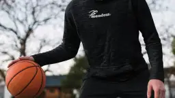 Mężczyzna w czarnej bluzie koszykarskiej z logo "Meadour" trzyma piłkę do koszykówki.