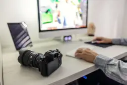 Aparat Sony leży obok komputera, gotowy do zgrania zdjęć. Na ekranie widać edytowane obrazy, a dłonie pracują przy klawiaturze.