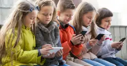 Dzieci skupione na ekranach telefonów i tabletu, szukają najlepszych gier dla 4 latka na telefon.