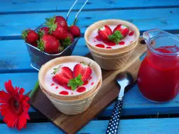 Panna cotta w wafelkach z truskawkami i miętą, obok dzbanuszek z musem truskawkowym.
