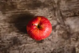 Czerwone jabłko z kroplami wody na drewnianym tle.