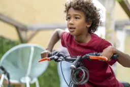 Chłopiec z kręconymi włosami na rowerze, trzymający kierownicę.