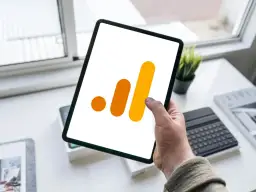 Ręka trzyma tablet z ikoną Google Analytics 4. Analiza zdarzeń GA4 na urządzeniu mobilnym.