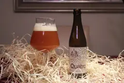 Szklanka i butelka piwa Quatro. Różnica między IPA a APA w doborze słodów i odmian chmielu jest kluczowa dla smaku.