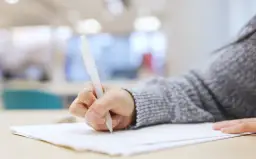 Dłoń pisze długopisem na kartce. Czy to próba przed maturą z angielskiego i ile słów na maturze z angielskiego?