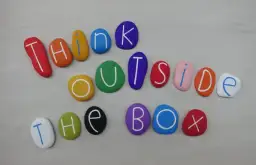 Kolorowe kamienie z literami tworzą napis "THINK OUTSIDE THE BOX". To jak polskie przysłowia po angielsku, zachęcające do nieszablonowego myślenia.