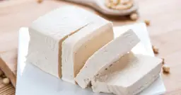 Kostka tofu, pokrojona w plastry, na białym talerzyku. Czy tofu to soja? Tak, to produkt z soi.