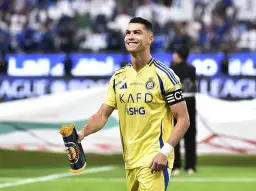 Uśmiechnięty Cristiano Ronaldo w żółtej koszulce Al Nassr, trzymający zwinięty szalik. Jego ogromne cristiano ronaldo zarobki budzą podziw.