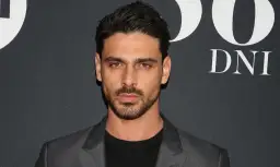 Michele Morrone w szarej marynarce i czarnej koszulce na tle napisu "DNI".