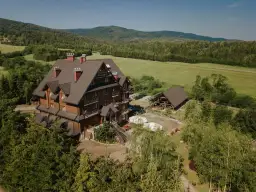 Hotel Carpatia Bieszczadzki Gościniec w otoczeniu zieleni, z drewnianym budynkiem i widokiem na góry.