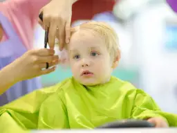 Mały chłopiec z blond włosami otrzymuje swoją pierwszą fryzurę. Włosy są delikatnie cięte, tworząc urocze fryzury dla rocznego chłopca.