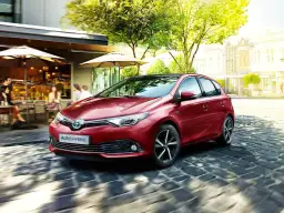 Czerwony Auris Hybrid, najbardziej ekonomiczne auto, sunie po brukowanej uliczce obok kawiarni.