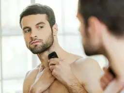 Mężczyzna goli szyję golarką, patrząc w lustro.