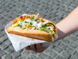Kebab w bułce z kurczakiem i wołowiną, z warzywami i serem feta, trzymany w dłoni.