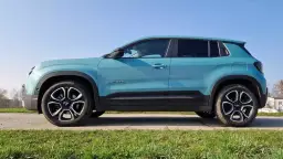 Turkusowy Jeep Avenger widziany z boku na tle nieba i zielonej trawy.
