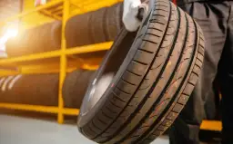 Opona samochodowa trzymana w rękawiczce na tle regału z oponami.