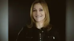 Uśmiechnięta blondynka w czarnej ramonesce na ciemnym tle.