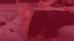 Dwie osoby siedzą naprzeciwko siebie, jedna pisze w notatniku, druga wskazuje palcem.