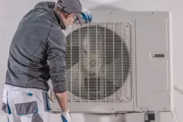 Technik w rękawiczkach sprawdza jednostkę zewnętrzną pompy ciepła, być może w celu diagnozy awarii pomp ciepła.