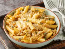 Makaron penne z karmelizowaną cebulą i roztopionym serem, ozdobiony tymiankiem.