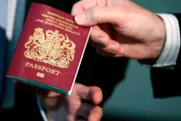 Dłoń podaje paszport biometryczny Wielkiej Brytanii. Widoczny herb i napis "PASSPORT".