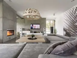 Nowoczesny salon z dominującym betonem w architekturze. Kominek, ściany i podłoga tworzą surową bazę dla przytulnych mebli.