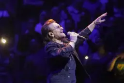 Bono z U2 śpiewa na koncercie, zapowiadając u2 nowa płyta. Tłum w ciemnościach reaguje na jego występ.